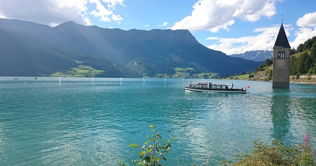 Il campanile sommerso di Curon che emerge dal Lago di Resia con un battello turistico